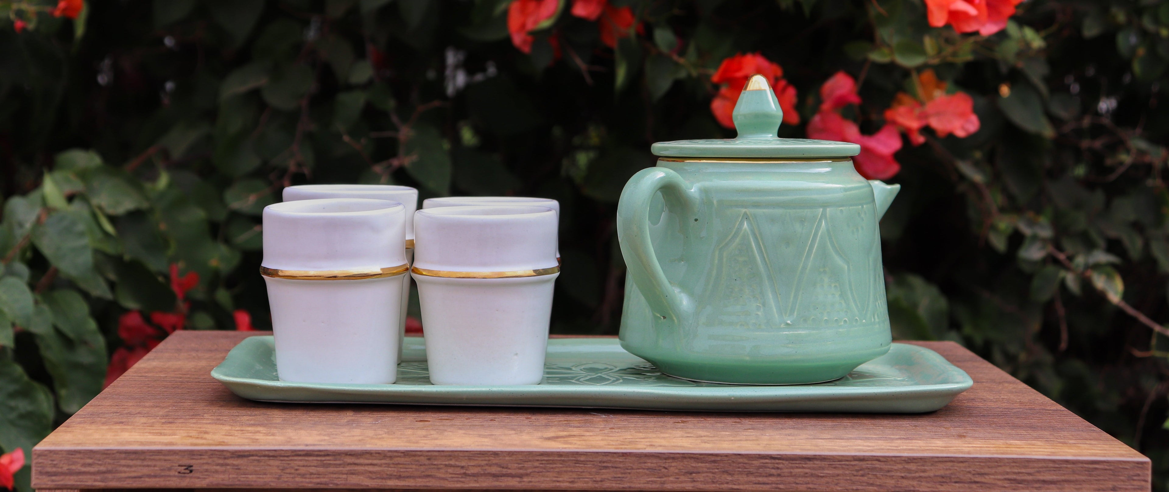 Green teapot and white cups on a tray with red flowers in the background